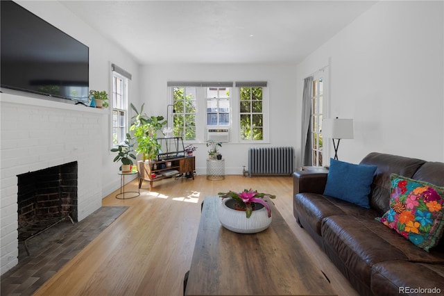 living room featuring radiator heating unit, hardwood / wood-style flooring, a brick fireplace, and cooling unit