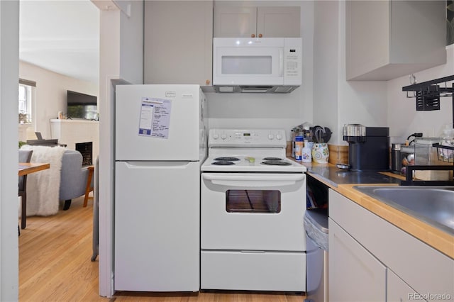 kitchen featuring light wood-type flooring, white appliances, and a fireplace