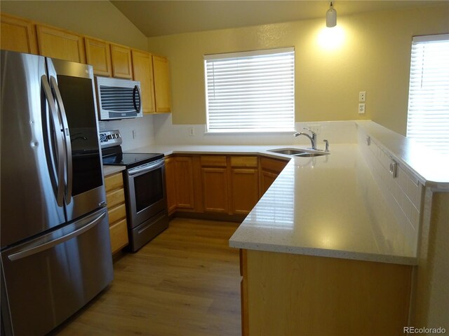 kitchen with appliances with stainless steel finishes, a sink, light wood finished floors, a peninsula, and lofted ceiling