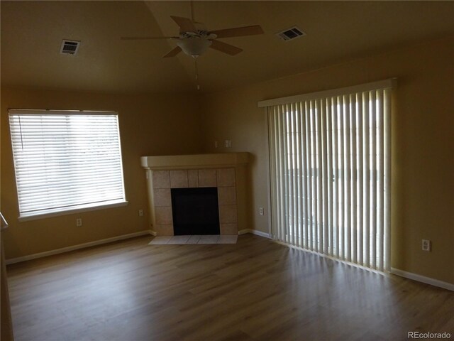 unfurnished living room with ceiling fan, wood finished floors, a tiled fireplace, baseboards, and vaulted ceiling