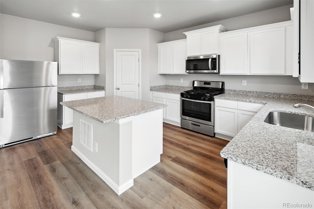 kitchen with sink, light stone counters, a center island, stainless steel appliances, and white cabinets