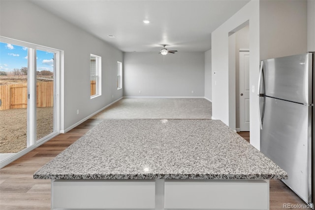 kitchen with stainless steel fridge, light hardwood / wood-style flooring, ceiling fan, white cabinetry, and light stone counters