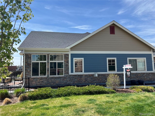 view of side of home featuring a lawn, stone siding, a shingled roof, and fence