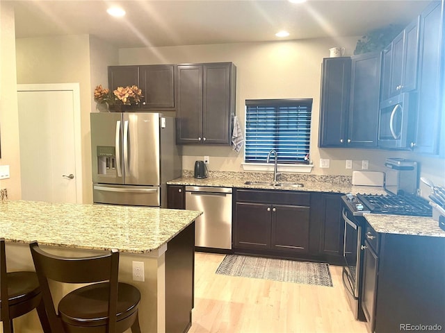 kitchen featuring a breakfast bar, light stone counters, light wood finished floors, a sink, and appliances with stainless steel finishes