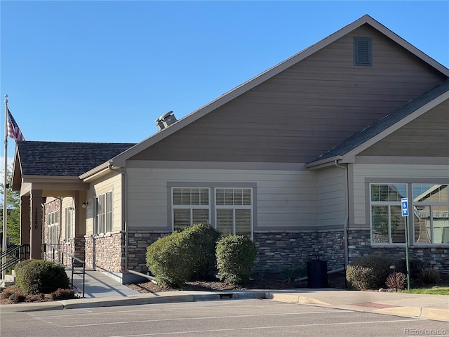 view of side of home with stone siding and a shingled roof