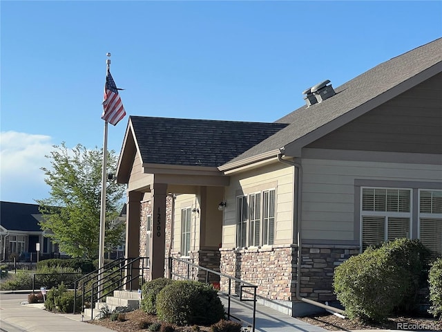 exterior space featuring stone siding and roof with shingles