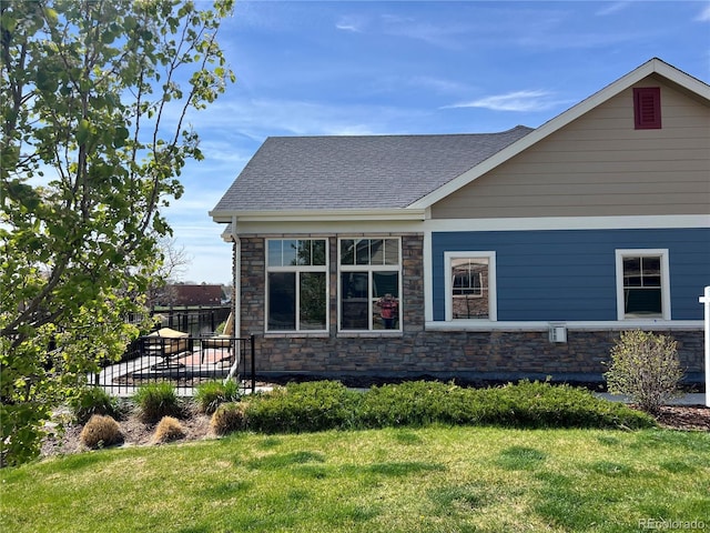 view of side of home with stone siding, a yard, roof with shingles, and fence