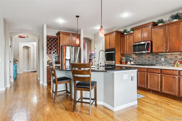 kitchen with hanging light fixtures, brown cabinetry, arched walkways, and stainless steel appliances