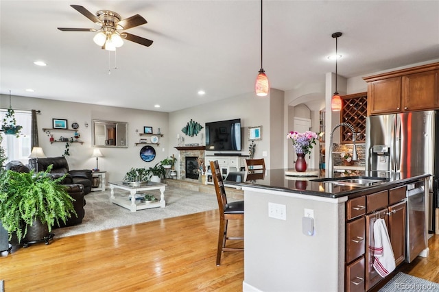 kitchen with dark countertops, open floor plan, arched walkways, and an island with sink