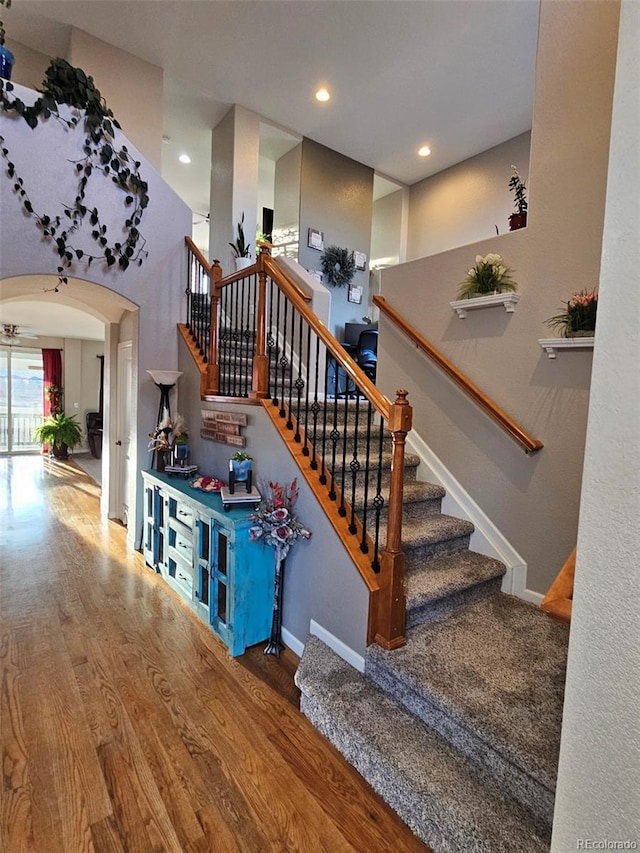 stairway with recessed lighting, arched walkways, baseboards, and wood finished floors