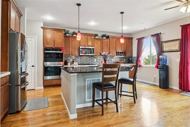 kitchen with light wood finished floors, stainless steel appliances, visible vents, ceiling fan, and tasteful backsplash