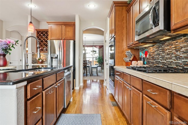 kitchen with a sink, arched walkways, light wood-style floors, stainless steel appliances, and tasteful backsplash