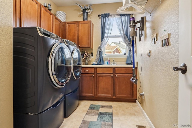 laundry room with light tile patterned floors, baseboards, washer and dryer, cabinet space, and a textured wall