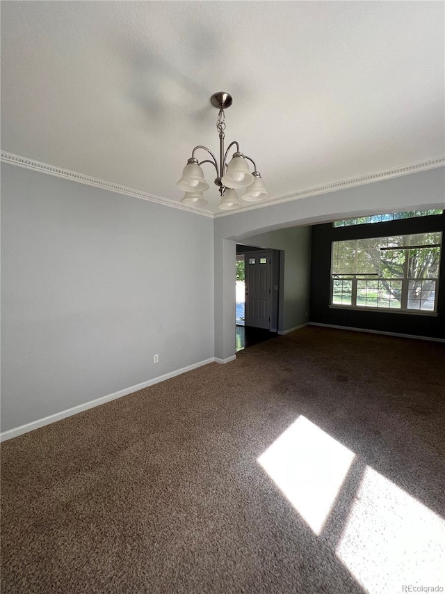 carpeted spare room featuring a notable chandelier, baseboards, and crown molding