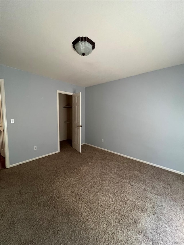 unfurnished bedroom featuring dark carpet, a closet, and a spacious closet