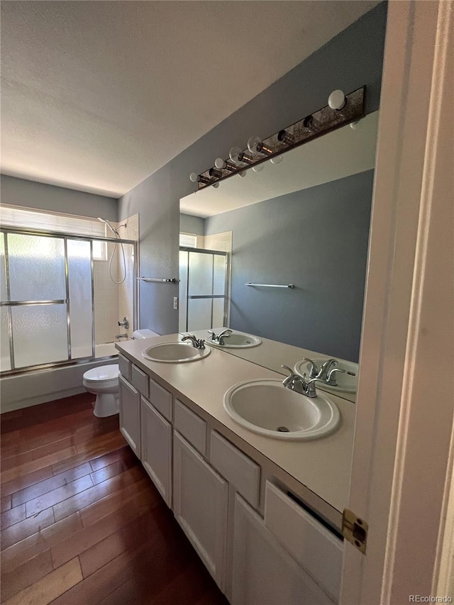 full bath with toilet, wood finished floors, a sink, and bath / shower combo with glass door