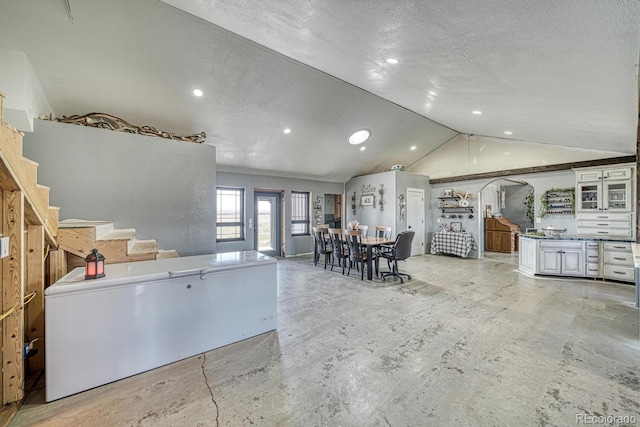kitchen with lofted ceiling, recessed lighting, concrete floors, a textured ceiling, and glass insert cabinets
