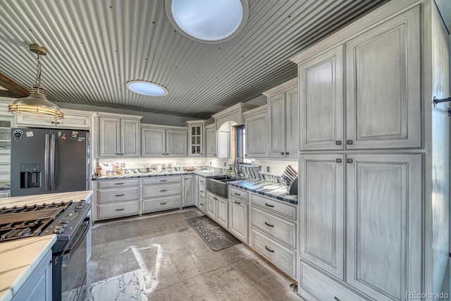 kitchen with light countertops, stainless steel refrigerator with ice dispenser, black gas range, a sink, and glass insert cabinets