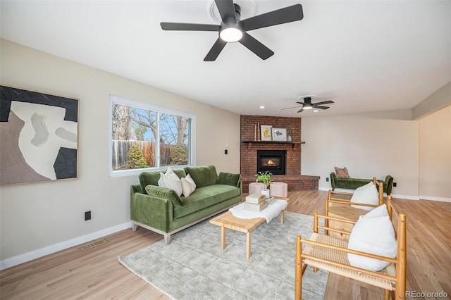 living room featuring visible vents, a brick fireplace, baseboards, ceiling fan, and wood finished floors