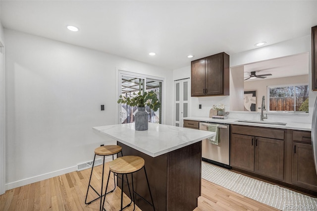 kitchen with a sink, a kitchen bar, light wood-type flooring, and dishwasher