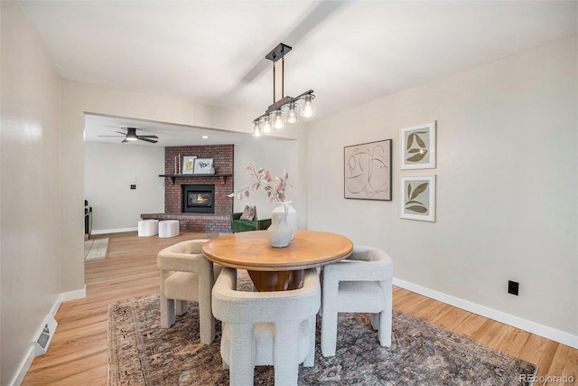 dining area with light wood-type flooring, visible vents, a ceiling fan, baseboards, and a brick fireplace