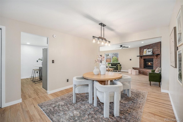 dining space with baseboards, a ceiling fan, a fireplace, and light wood finished floors