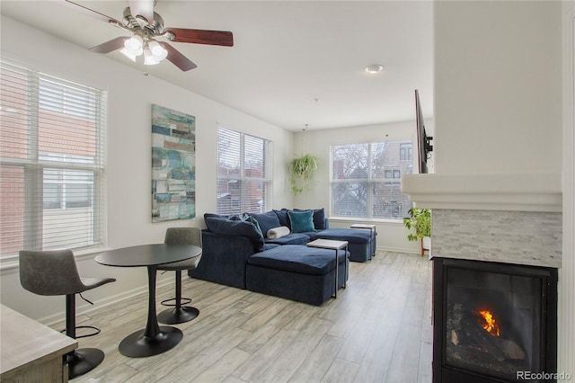 living room featuring ceiling fan, a stone fireplace, light wood-type flooring, and a wealth of natural light