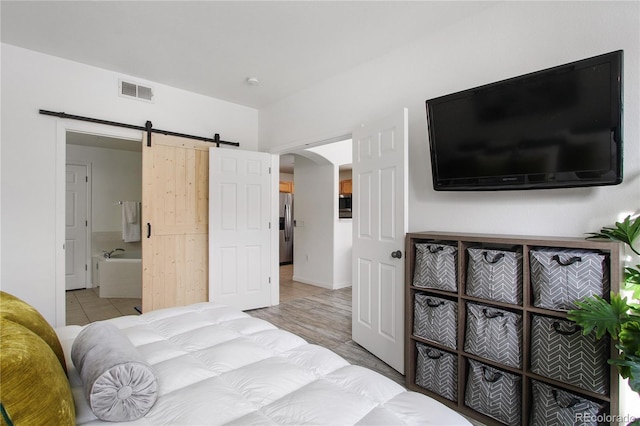 bedroom featuring ensuite bathroom, a barn door, stainless steel fridge with ice dispenser, and light tile patterned floors