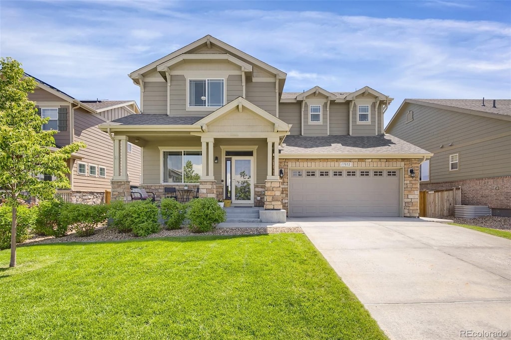 17052 Lipan St, Broomfield, CO 80023 - craftsman house with covered porch, a front yard, concrete driveway, an attached garage, and stone siding