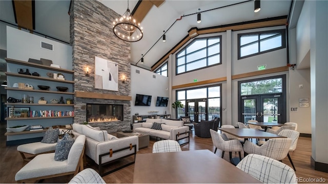 living room with french doors, wood-type flooring, a notable chandelier, a high ceiling, and a stone fireplace