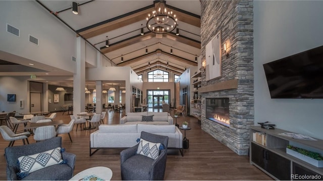 interior space featuring a stone fireplace, wood-type flooring, high vaulted ceiling, and an inviting chandelier