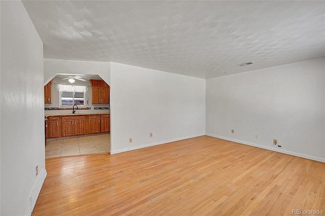 unfurnished living room with sink, light hardwood / wood-style flooring, a textured ceiling, and ceiling fan