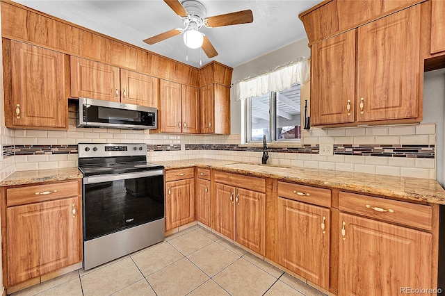 kitchen featuring sink, tasteful backsplash, light stone counters, light tile patterned floors, and appliances with stainless steel finishes