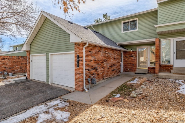 view of side of property with driveway, an attached garage, a shingled roof, entry steps, and brick siding