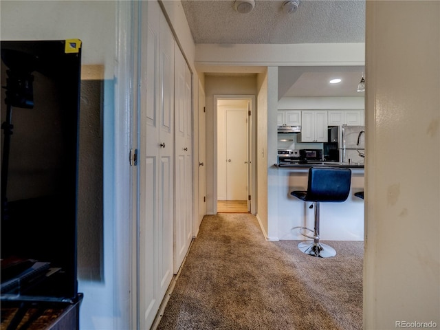 14590 E 2nd Ave Unit 105B, Aurora, CO 80011 - kitchen featuring freestanding refrigerator, carpet floors, white cabinets, dark countertops, and under cabinet range hood
