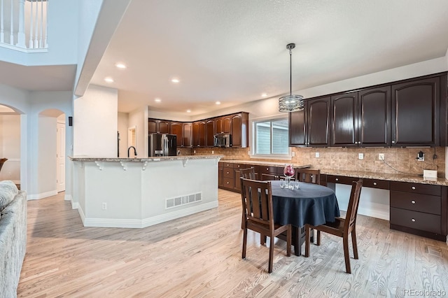 kitchen featuring dark brown cabinets, light wood-type flooring, hanging light fixtures, stainless steel appliances, and backsplash