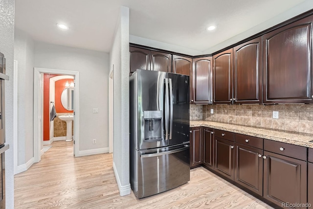 kitchen with backsplash, dark brown cabinets, stainless steel refrigerator with ice dispenser, light stone counters, and light hardwood / wood-style floors