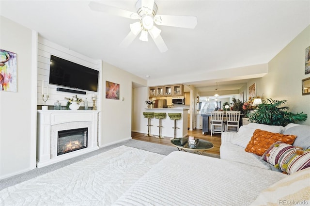 interior space with a glass covered fireplace, ceiling fan, light wood finished floors, and baseboards