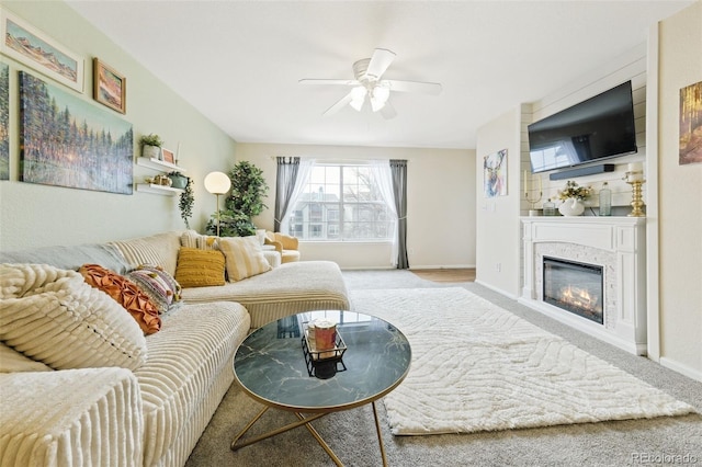 living area featuring light carpet, ceiling fan, baseboards, and a glass covered fireplace