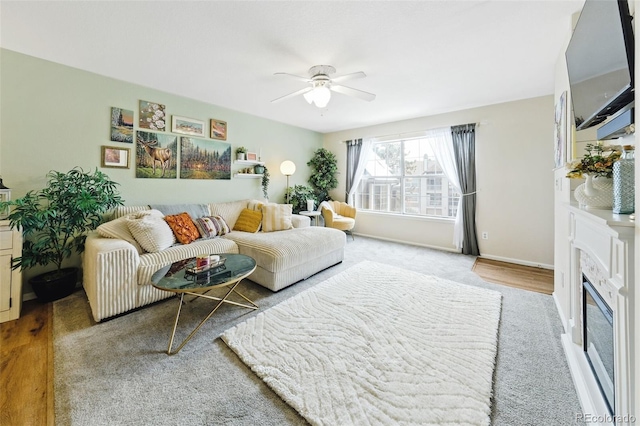 living area featuring baseboards, a ceiling fan, and a glass covered fireplace