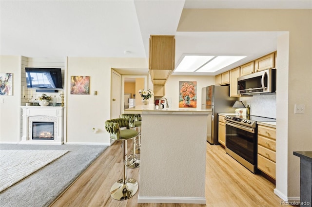 kitchen featuring stainless steel appliances, light countertops, open floor plan, light brown cabinets, and a kitchen breakfast bar