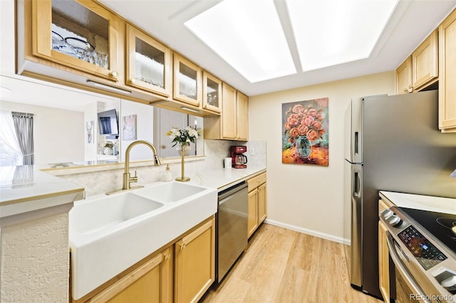 kitchen with a sink, light countertops, appliances with stainless steel finishes, light wood-type flooring, and glass insert cabinets