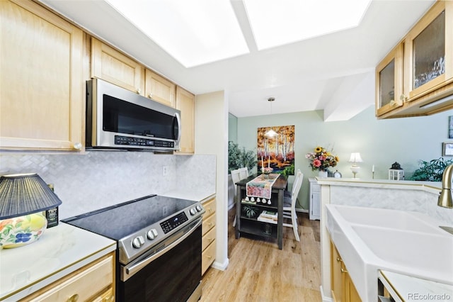 kitchen featuring glass insert cabinets, appliances with stainless steel finishes, decorative light fixtures, light countertops, and a sink