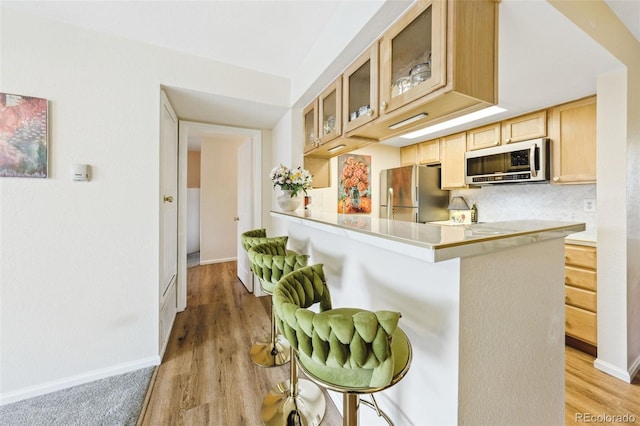 kitchen featuring a breakfast bar area, light countertops, glass insert cabinets, freestanding refrigerator, and a peninsula