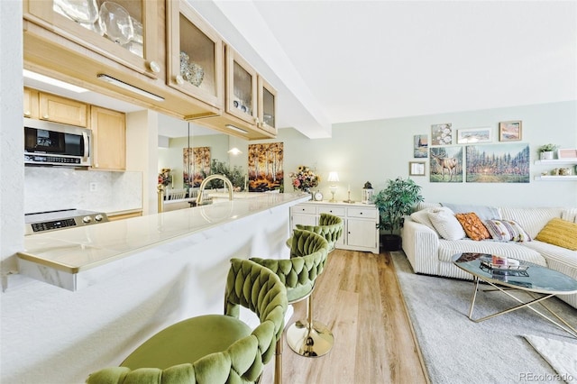 kitchen featuring a breakfast bar area, stainless steel microwave, backsplash, glass insert cabinets, and light wood-style floors