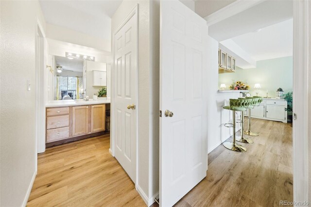 corridor featuring light wood finished floors, a sink, and baseboards