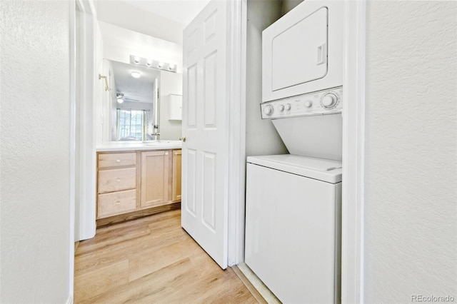 laundry room featuring stacked washer and dryer, a textured wall, laundry area, and light wood-style floors