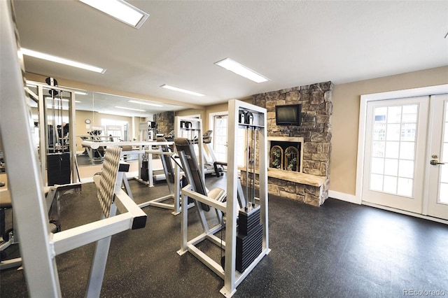 gym featuring a textured ceiling, baseboards, a stone fireplace, and french doors