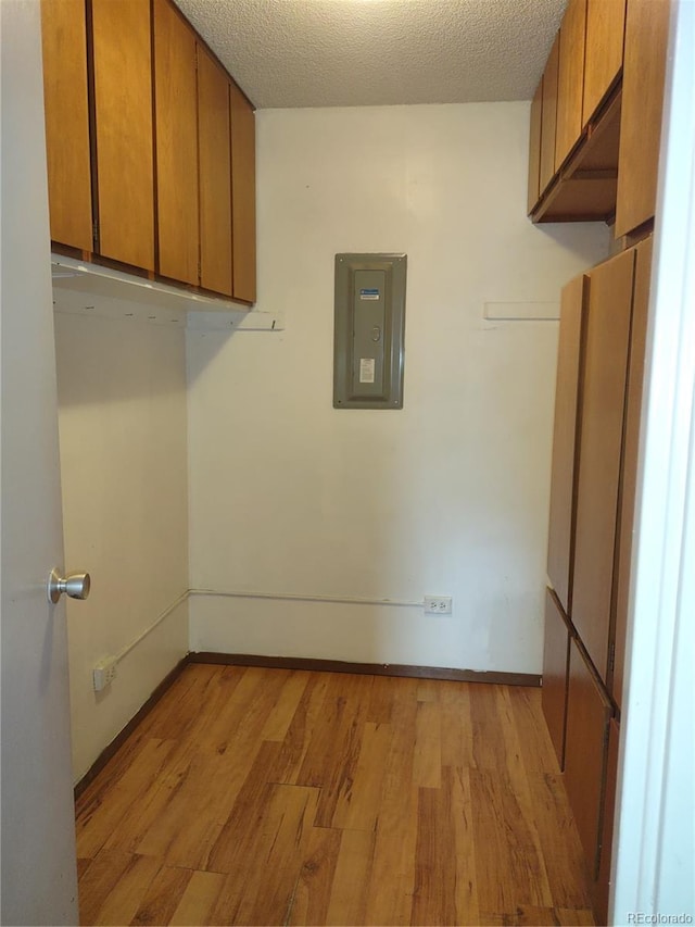 clothes washing area featuring light hardwood / wood-style flooring, electric panel, and a textured ceiling