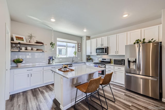 kitchen with tasteful backsplash, white cabinetry, wood-type flooring, a center island, and stainless steel appliances